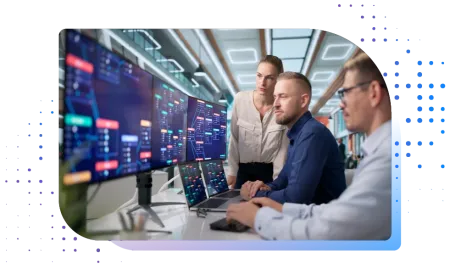 Three IT professionals analyzing complex data charts and system workflows across multiple screens in an office.