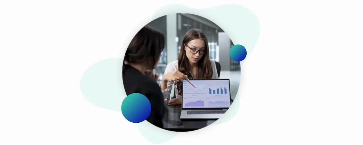 Two women analyzing financial charts and data on a laptop screen in a professional office setting.