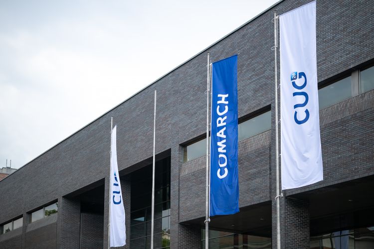 Comarch and CUG 26&nbsp;branding flags waving in&nbsp;front of&nbsp;the modern company building.