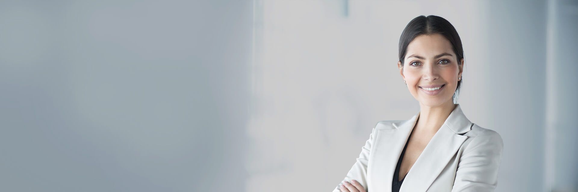 Smiling businesswoman with arms crossed in a light-colored blazer against a blurred office backgroun