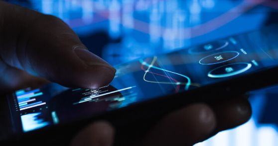 Hand interacting with smartphone displaying data analytics and graphs on a blue background.